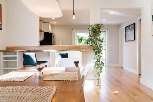 Bright, modern dining area with wooden table, plants, and open kitchen in a cozy, inviting space.
