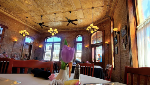 Cozy restaurant interior with brick walls, ornate ceiling, and a table set with a vase of tulips and menus.