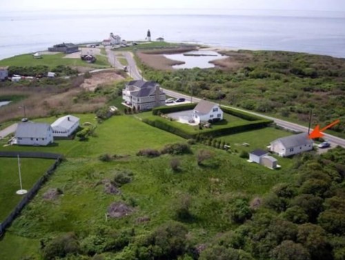 Aerial view of a coastal area with houses, greenery, and a road leading to the water in the background.