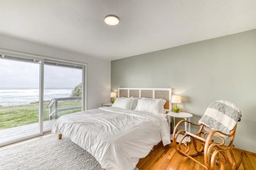 Cozy bedroom with a large bed, rocking chair, and ocean view through sliding glass doors.