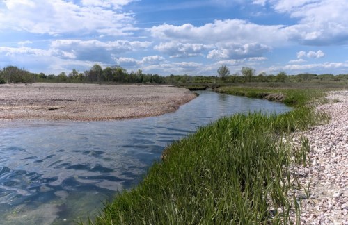 A serene river winding through a grassy landscape under a blue sky with fluffy clouds.