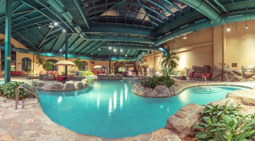 Indoor pool area featuring a tropical theme, rock formations, and lounge chairs under a high, blue ceiling.