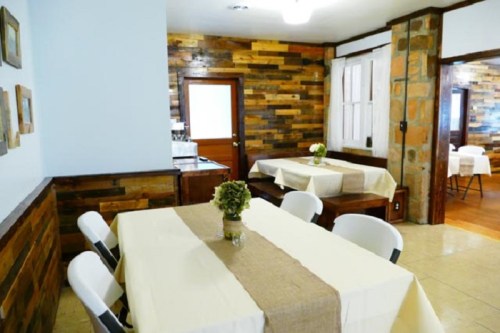 Cozy dining area with wooden walls, tables set with beige tablecloths, and a small vase of flowers on each table.