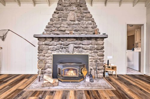 A cozy stone fireplace with a wood stove, surrounded by wooden flooring and a simple, rustic interior.