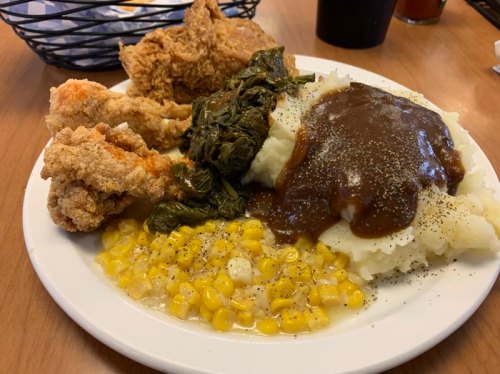 A plate of fried chicken, collard greens, mashed potatoes with gravy, and corn.