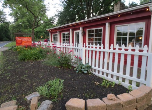 A charming red building with white trim and a picket fence, surrounded by greenery and flowers.