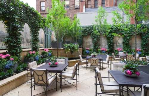 A serene outdoor patio with tables, chairs, and vibrant flowers surrounded by lush greenery and ivy-covered walls.