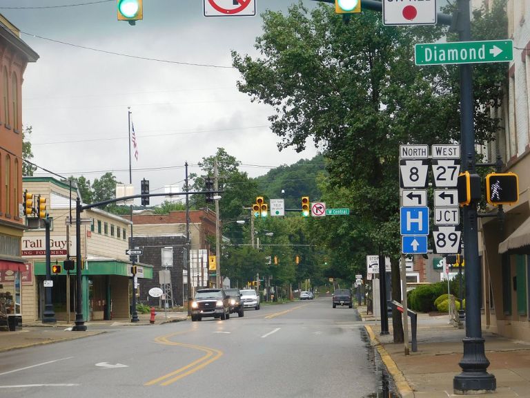 A street view showing traffic lights, directional signs, and storefronts under a cloudy sky.