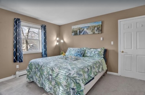 Cozy bedroom with a large bed, decorative pillows, and a nature-themed painting on the wall. Bright natural light.