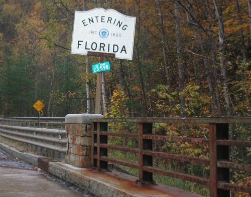 Sign marking the entrance to Florida, surrounded by trees with autumn foliage. Roadway visible in the foreground.