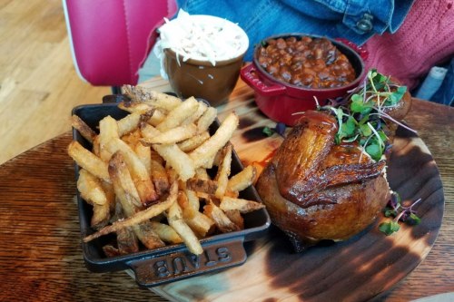 A plate featuring crispy fries, baked chicken, coleslaw, and baked beans on a wooden surface.