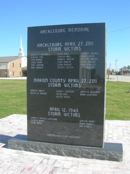 A black memorial stone listing storm victims from Hackleburg and Marion County, with names and dates inscribed.