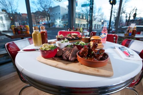 A table set with a variety of barbecue dishes, including meats, sides, sauces, and a burger, in a cozy restaurant.