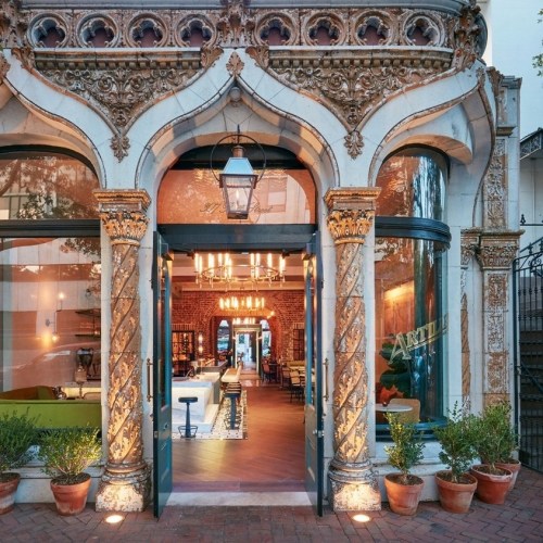 A beautifully ornate entrance with intricate architecture, leading into a stylish interior with warm lighting and greenery.