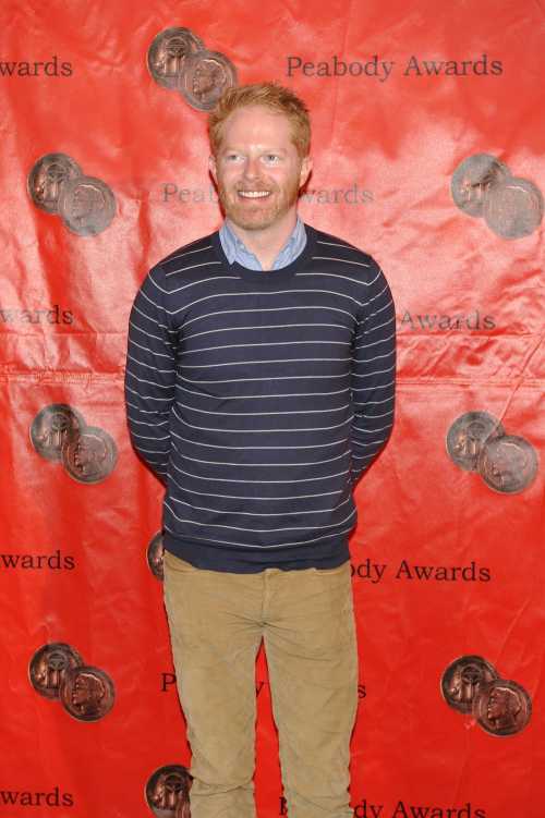 A smiling man in a striped sweater stands in front of a red backdrop with Peabody Awards logos.