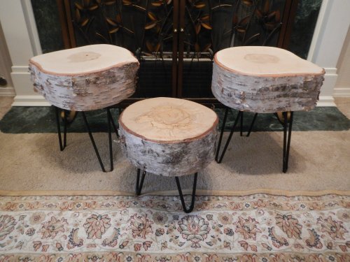 Three rustic wooden stools with natural edges and black metal legs, placed on a patterned rug near a fireplace.