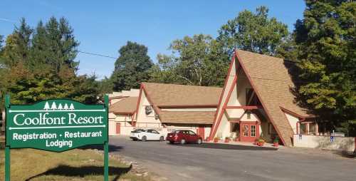 A view of Coolfont Resort featuring a lodge with a sign for registration, restaurant, and lodging. Trees in the background.