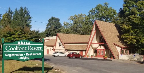 A view of Coolfont Resort featuring a lodge with a sign for registration, restaurant, and lodging. Trees in the background.