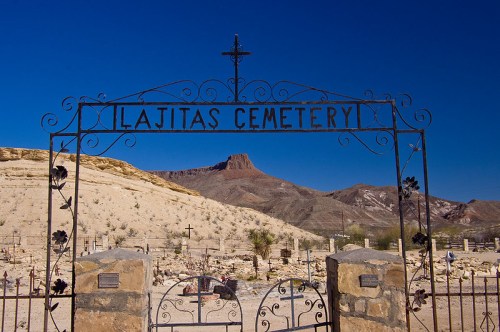 Wrought iron gate of Lajitas Cemetery with a mountain backdrop under a clear blue sky.