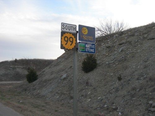 Signpost indicating "South 99" and "Scenic Byway" with "Native Stone" information, set against a hilly landscape.