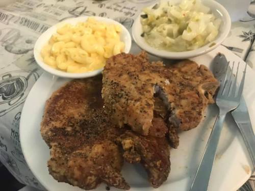 A plate of fried pork chops with seasoned crust, served with macaroni and cheese and coleslaw on the side.