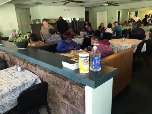 A busy dining area with people eating at tables, a counter in the foreground, and hand sanitizer visible.