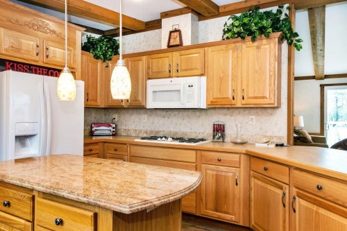 Bright kitchen with wooden cabinets, granite countertops, and pendant lights, featuring a microwave and gas stove.