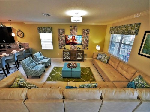 Cozy living room with a large sectional sofa, colorful decor, and a TV on the wall, featuring a bright, inviting atmosphere.