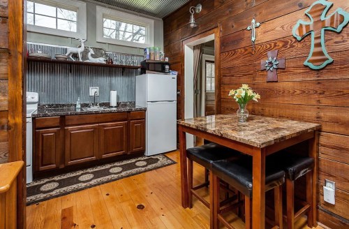 Cozy kitchen with wooden walls, a marble-top table, and a small dining area featuring a vase of flowers.