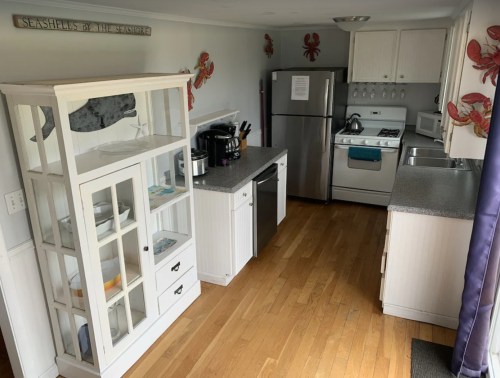 A bright kitchen featuring a glass-front cabinet, stainless steel appliances, and wooden flooring. Decorated with crab motifs.