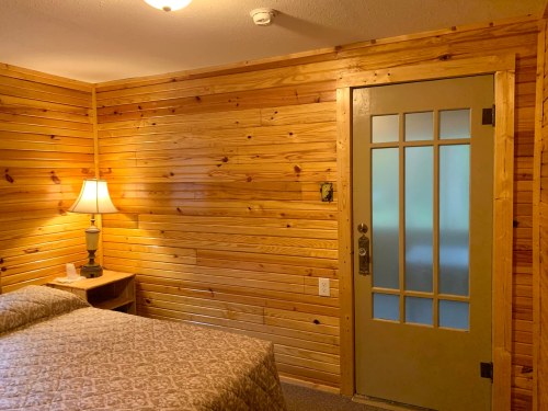 Cozy room with wooden walls, a bed, a lamp on a nightstand, and a frosted glass door.