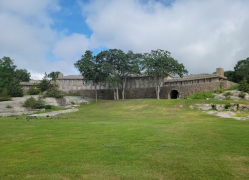 A large stone building surrounded by trees and grassy land under a cloudy sky.