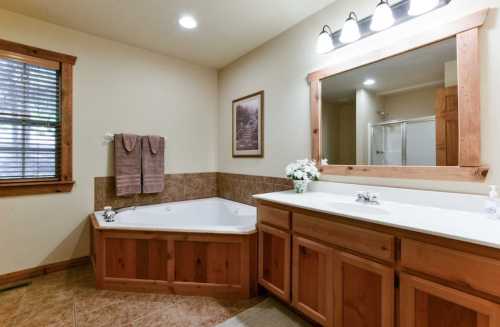 Spacious bathroom featuring a jetted tub, double vanity, and natural wood accents. Bright lighting and a mirror above the sink.