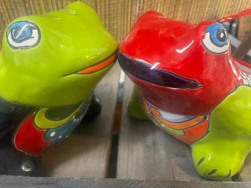 Two colorful ceramic frogs, one green and one red, face each other with playful expressions.