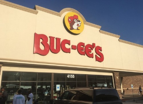 Exterior of a Buc-ee's store with a large sign and people in front, under a clear blue sky.