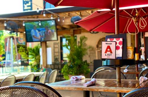 Outdoor dining area with red umbrellas, a menu on the table, and a TV screen in the background showing a program.