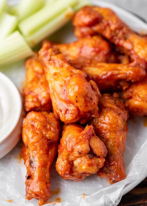 A plate of spicy chicken wings with celery sticks and a small bowl of dipping sauce.