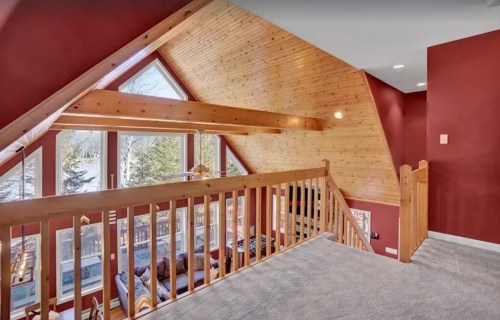 A cozy loft area with wooden beams, red walls, and large windows overlooking a scenic view.