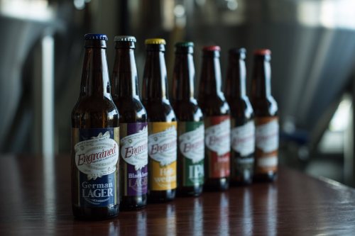 A lineup of beer bottles on a wooden table, featuring various styles like German Lager and IPA.