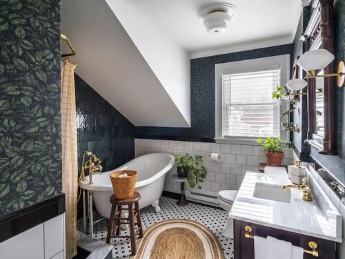 A stylish bathroom featuring a freestanding tub, dark floral wallpaper, and a mix of modern and vintage decor.