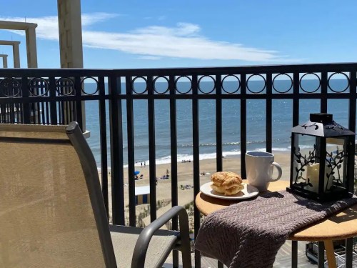 A balcony view overlooking the beach, with a cup of coffee, pastries, and a lantern on a small table.