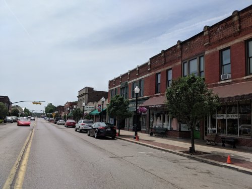 A quiet street lined with brick buildings, shops, and parked cars under a cloudy sky.