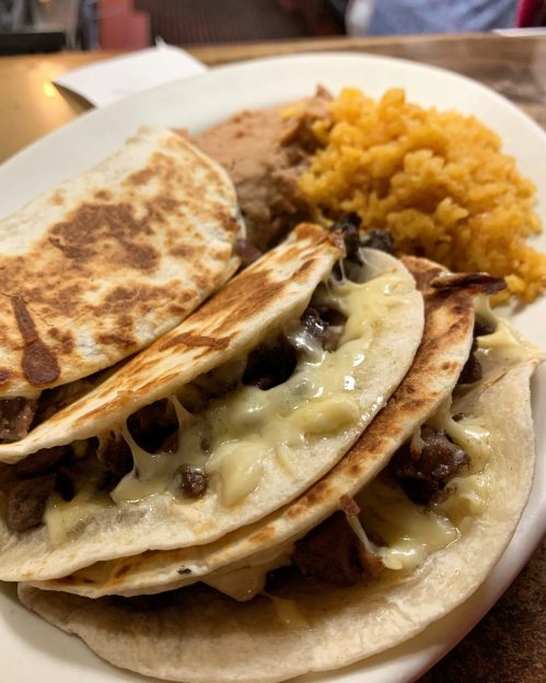 Three cheesy tacos filled with beef, served with rice and refried beans on a white plate.