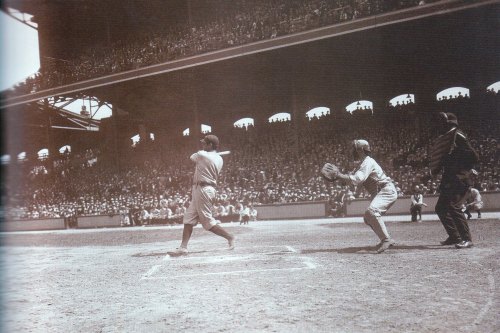 A historic baseball game scene with a batter swinging, a catcher ready, and a large crowd in the stands.