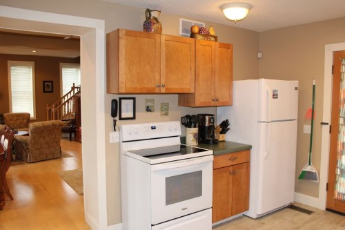 A cozy kitchen with wooden cabinets, a white stove, and a refrigerator, leading to a living area with a sofa.