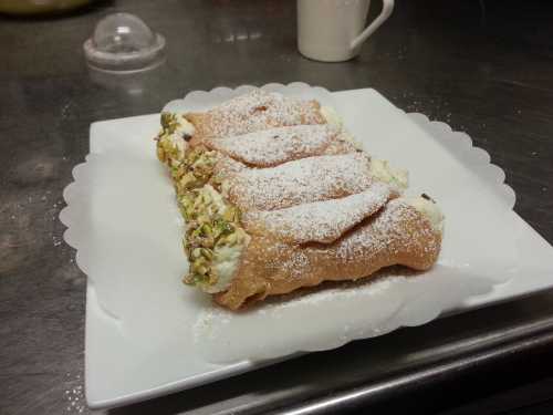 A plate of cannoli filled with cream and topped with powdered sugar and pistachios.