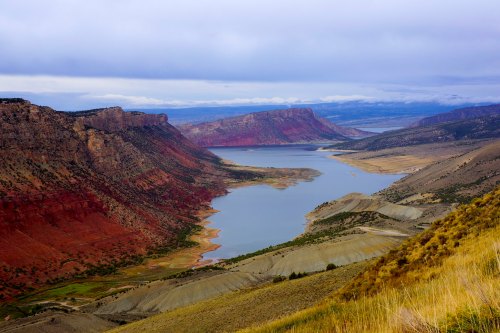 A scenic view of a winding river surrounded by red and gray cliffs under a cloudy sky.