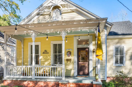 A charming yellow house with a porch, decorative trim, and string lights, inviting and well-maintained.