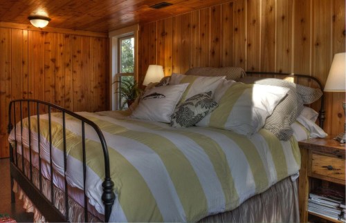 Cozy bedroom with a wooden wall, featuring a large bed with striped bedding and bedside lamps.