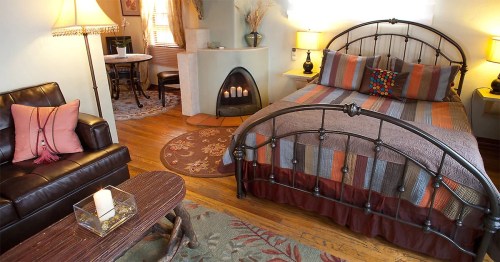 Cozy bedroom with a metal bed, colorful bedding, a fireplace, and a seating area with a leather couch and table.